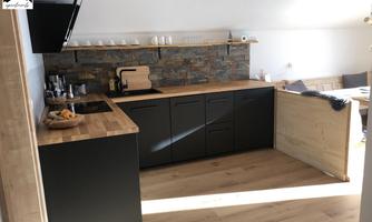 A modern kitchen with a wooden countertop and dark cabinets. The room has plenty of natural light and a cozy atmosphere.