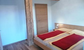 A cozy bedroom with a double bed and red blankets. The walls are light, and a wooden post gives the room a rustic charm.
