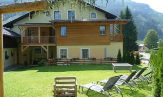 A charming house with wooden cladding in the midst of a green meadow. In the foreground, there are lounge chairs for relaxing.