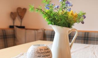 A beautiful table with a white pitcher full of fresh flowers and a decorative stone with a motivational inscription. The surroundings are cozy and inviting.
