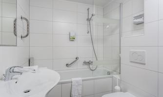 A modern bathroom with white tiles and a shower. There is a sink, a toilet, and towels made of white fabric.