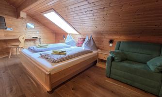 A cozy bedroom with wood paneling and a skylight. The room is furnished with a double bed, an armchair, and a desk.