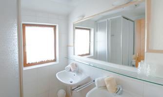 A modern bathroom with a large mirror surface. It features a sink, some towels, and a shower.