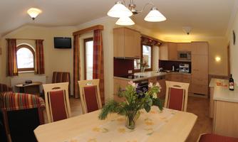A modern kitchen with a dining area and cozy living room. The rooms are bright and friendly with wooden cabinets and a flower arrangement on the table.