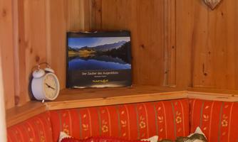 A cozy corner with wooden walls, a red upholstered bench, and decorative cushions. In the background, there is a calendar with a landscape picture and a clock visible.