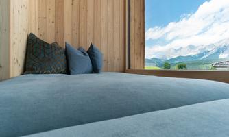 A modern bedroom with a low bed and soft pillows. A stunning mountain landscape is visible through the large window.