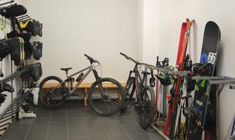 A spacious storage room with bicycles and ski equipment. The walls are adorned with ski boots and various sports equipment.