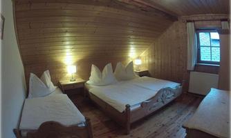 A cozy bedroom with two beds and wooden interiors. The walls have a warm wood paneling and there are two nightstands with lamps.