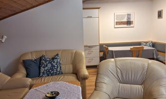 A cozy living room with comfortable sofas and a wooden table. The room has a warm atmosphere with a wooden ceiling and modern furnishings.
