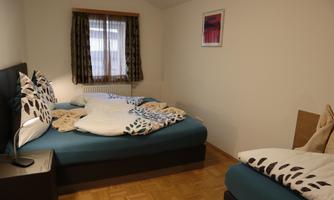 A cozy bedroom with two beds and modern decorations. The windows have curtains, and a picture hangs on the wall.
