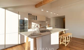 A modern kitchen with a light wooden floor and white cabinets. The large kitchen island provides space for cooking and dining.
