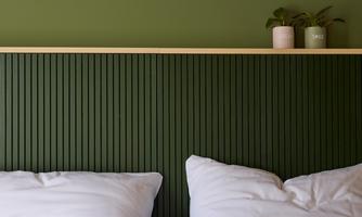 A modern bedroom with a green wall area and two white pillows. There are plants and candles on the wall shelf.