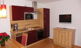 A modern kitchen with wooden and red cabinets. It is equipped with a stove, a sink, and a television on the wall.