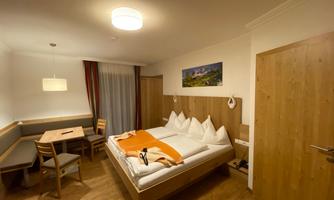 A cozy hotel room with a double bed and wooden interior. There is a table and chairs as well as a window front with curtains.