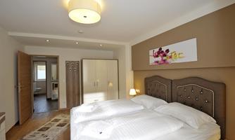 A modern bedroom with a comfortable double bed and elegant decoration. The walls are painted in gentle colors, and there is a large wardrobe as well as a door to an adjoining room.