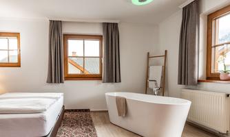 A modern room with a cozy bed and a freestanding bathtub. Large windows provide plenty of natural light and an inviting atmosphere.