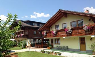 Two rustic houses with flower boxes and a well-maintained garden. The sky is blue with a few clouds.