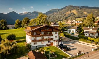 A traditional house in a picturesque setting with green meadows and mountains in the background. The architecture is typical for the Alpine region.