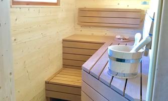 A cozy sauna with light wooden paneling and benches. A bucket and a ladle are available.