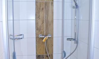A modern shower with smooth tiles and a wooden cladding. The showerhead and fittings are made of stainless steel.