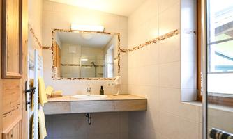 A modern bathroom with a bright tiled floor and wooden details. The large mirror above the sink reflects a pleasant atmosphere.