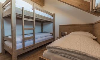 A cozy bedroom with a bunk bed and a single bed. The walls and furniture are made of light wood, creating a warm atmosphere.