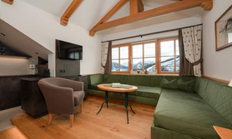 A cozy living and dining room with a green couch and a round table. Large windows offer a view of the snow-covered mountains.