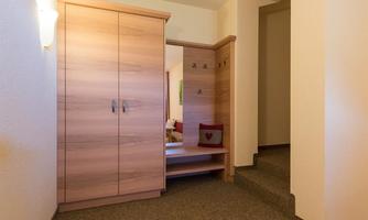 A bright hallway with a wooden cupboard and a step. On the left side, there is a seating area.