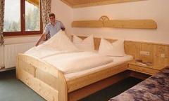 A cozy room with a large wooden bed and white bedding. One person is making the bed and creating an inviting atmosphere.
