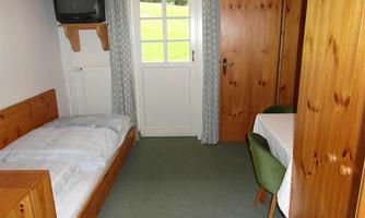 A simple room with a single bed, a table, and two chairs. There is a window with a view outside and a television.