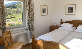 A cozy bedroom with a wooden bed and a desk. Through the window, there is a view of the green landscape.