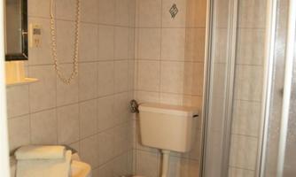 A small bathroom with a shower, toilet, and sink. The walls are tiled, and the furnishings are simple.