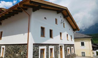 A traditional house with white plaster and a stone base. The eaves and the windows give the building a rustic charm.