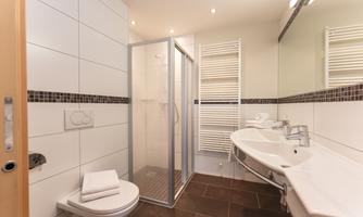 A modern bathroom with a shower and a sink. The walls are brightly tiled and there is a towel holder.