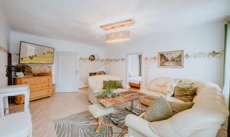 A stylish living room with beige sofas and a wooden table. The walls are decorated with pictures, and there are plants for a cozy atmosphere.