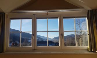 A view through a large window of a hilly landscape. The mountain backdrop is clear and radiant in the sunlight.