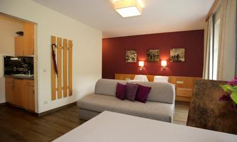 A cozy room with a sleeping area and a small living area. The purple cushions and warm lighting create an inviting atmosphere.