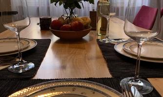 A beautifully set table with elegant plates and glasses. In the center stands a flower vase and a fruit bowl.