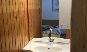 A small bathroom with wooden paneling and a modern sink. A mirror and a window provide brightness in the room.