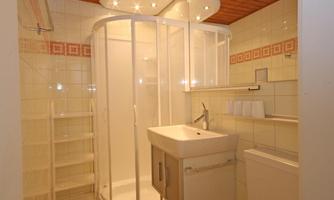 A modern bathroom with a shower cabin and a sink. The walls are tiled and there is bright ceiling lighting.