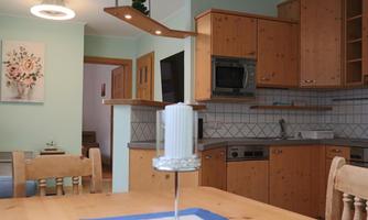 A cozy kitchen with wooden cabinets and a dining area. In the middle, there is a candle on a table with a blue tablecloth.