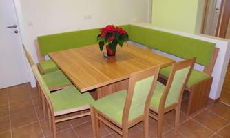 A modern dining area with a large rectangular table and chairs. Against one wall, there is a cozy bench with green cushions.