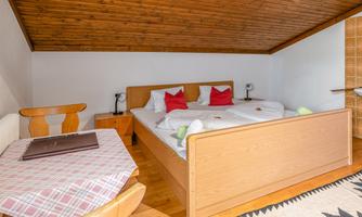 A cozy bedroom with a double bed and wooden floor. A small table and chairs complement the room.