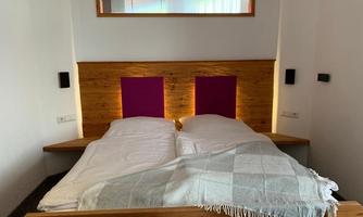 A cozy bedroom with a double bed and wooden elements. The wall behind the bed is designed in soft colors.