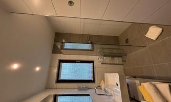 A modern bathroom with a walk-in shower and a simple sink. Bright tiles and large windows create a friendly atmosphere.