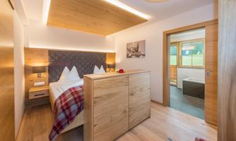 A modern bedroom with wood details and a cozy bed area. The room features windows overlooking nature and a tranquil atmosphere.