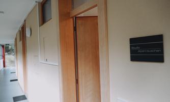 A hallway with beige walls and a wooden door. On the wall is a sign that reads "Studio Abnehmstudio".