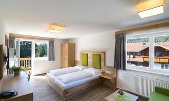 A bright, modern room with two beds and a large window. The room is decorated with wooden furniture and a small table.