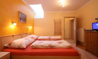 A cozy bedroom with a large bed and orange walls. In the room, there is a television and a window for daylight.
