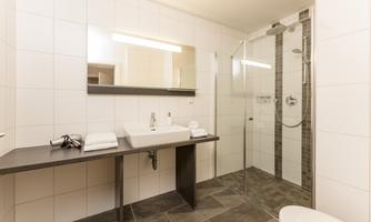 A modern bathroom with an open shower and a large mirror. The walls are brightly tiled and the floor is a dark color.